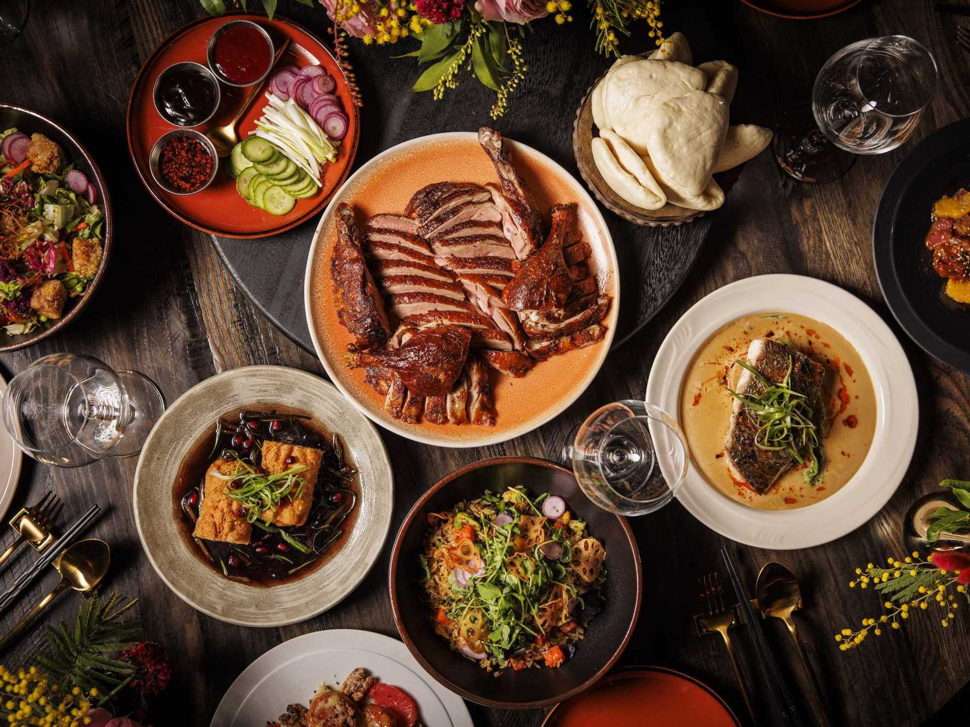A table spread at Night Rooster with tea smoked duck, noodles, and steamed redfish