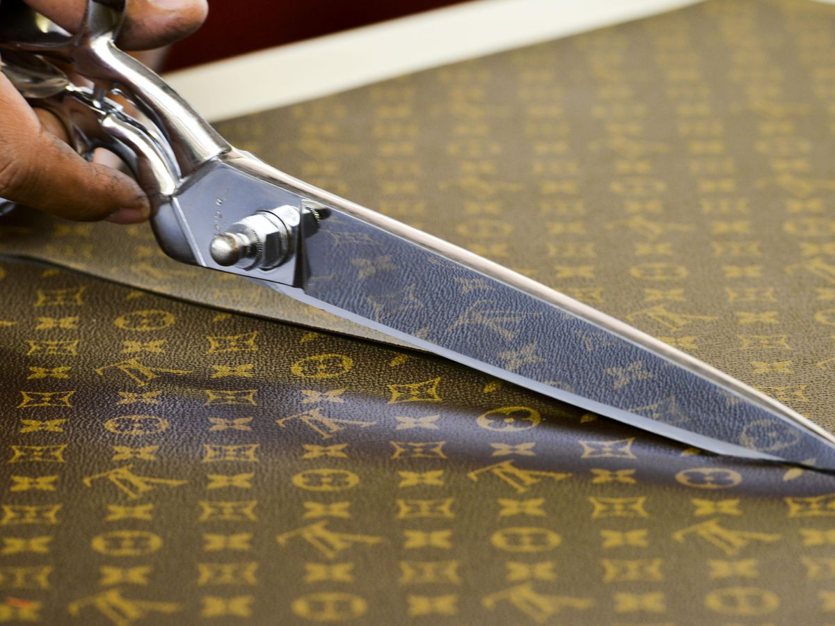 A worker cuts the distinctive LV logo fabric of natural cowhide leather  without using a ruler. He says he has been on the job here since 1988. The  interlocking chocolate brown and