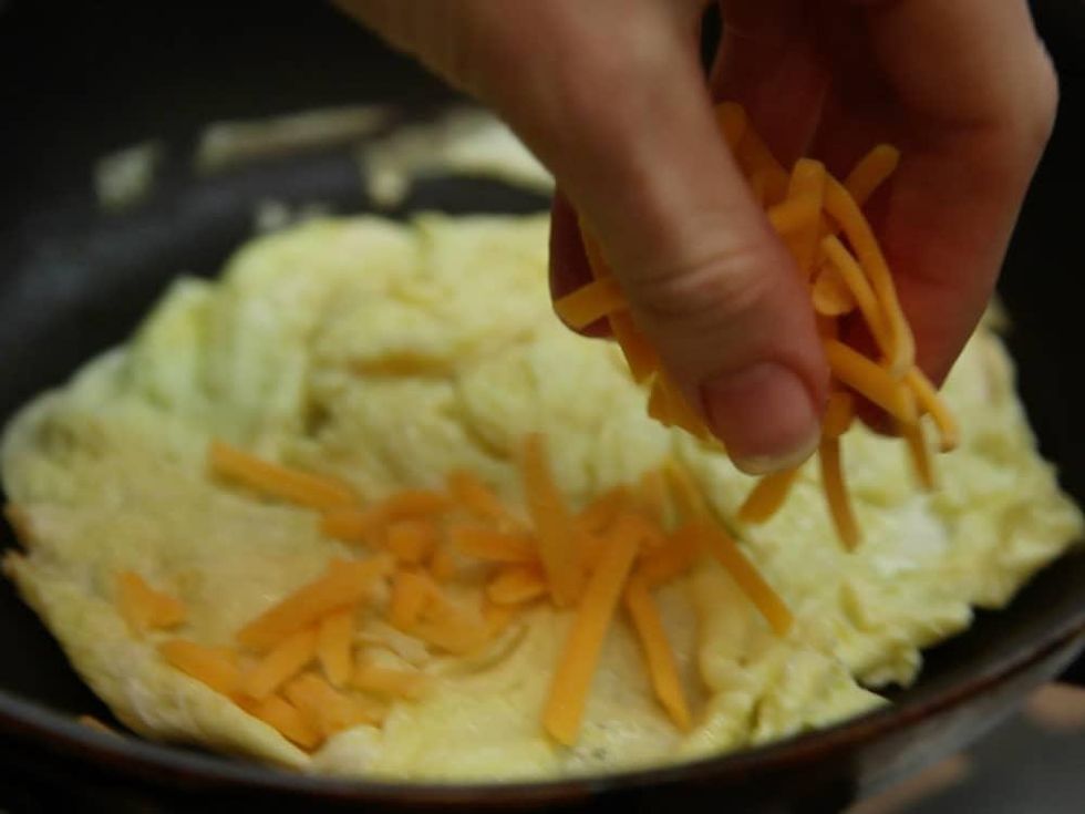 Adding shredded cheese to an omelet