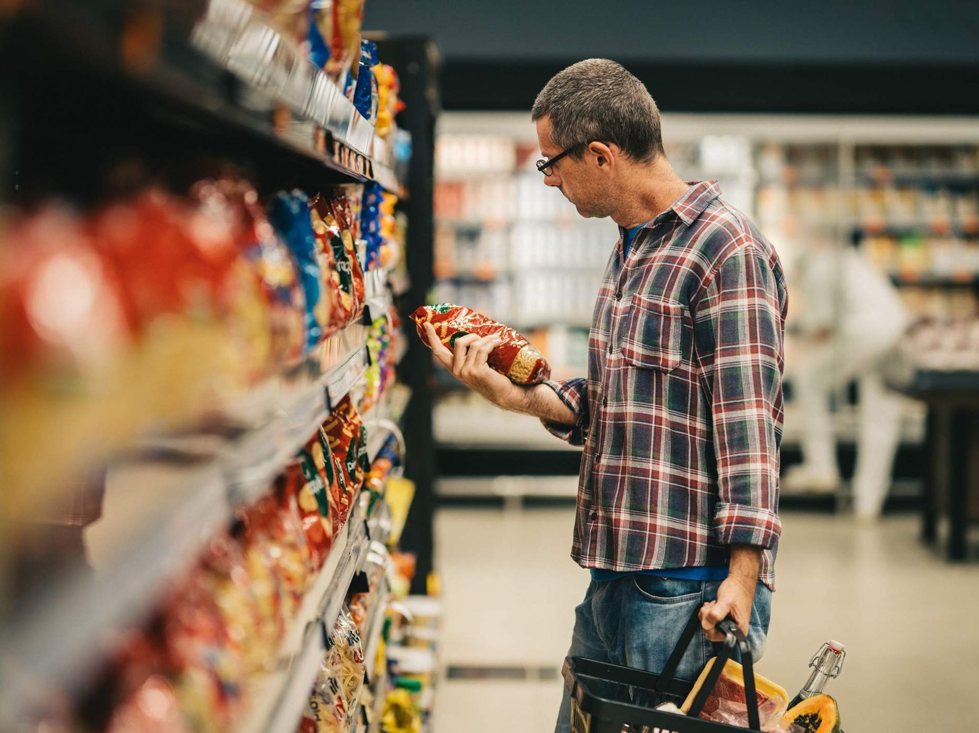 Man reading a label while grocery shopping in a supermarket aisle