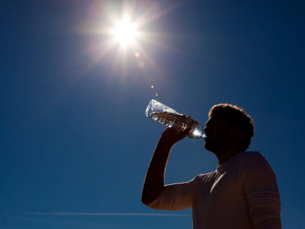 silhouette of man drinking water in hot sun blue sky